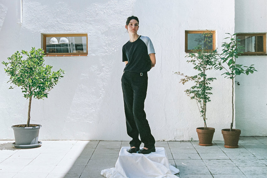 Lifestyle photo of a person wearing Mary Jane Calfskin Black shoes with dark trousers, standing in a room with plants and framed art