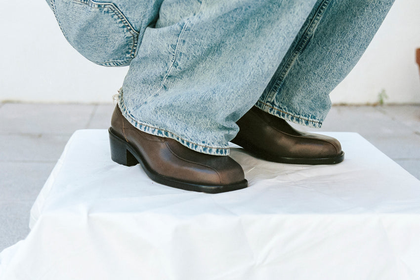 Lifestyle close-up of feet wearing Pedal Loafer Oil Nappa Mud shoes with light-wash denim jeans