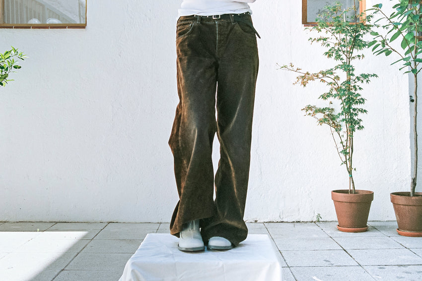 Lifestyle photo of a person wearing Cove Boot Nubuck Perla boots with olive trousers, standing near a potted plant