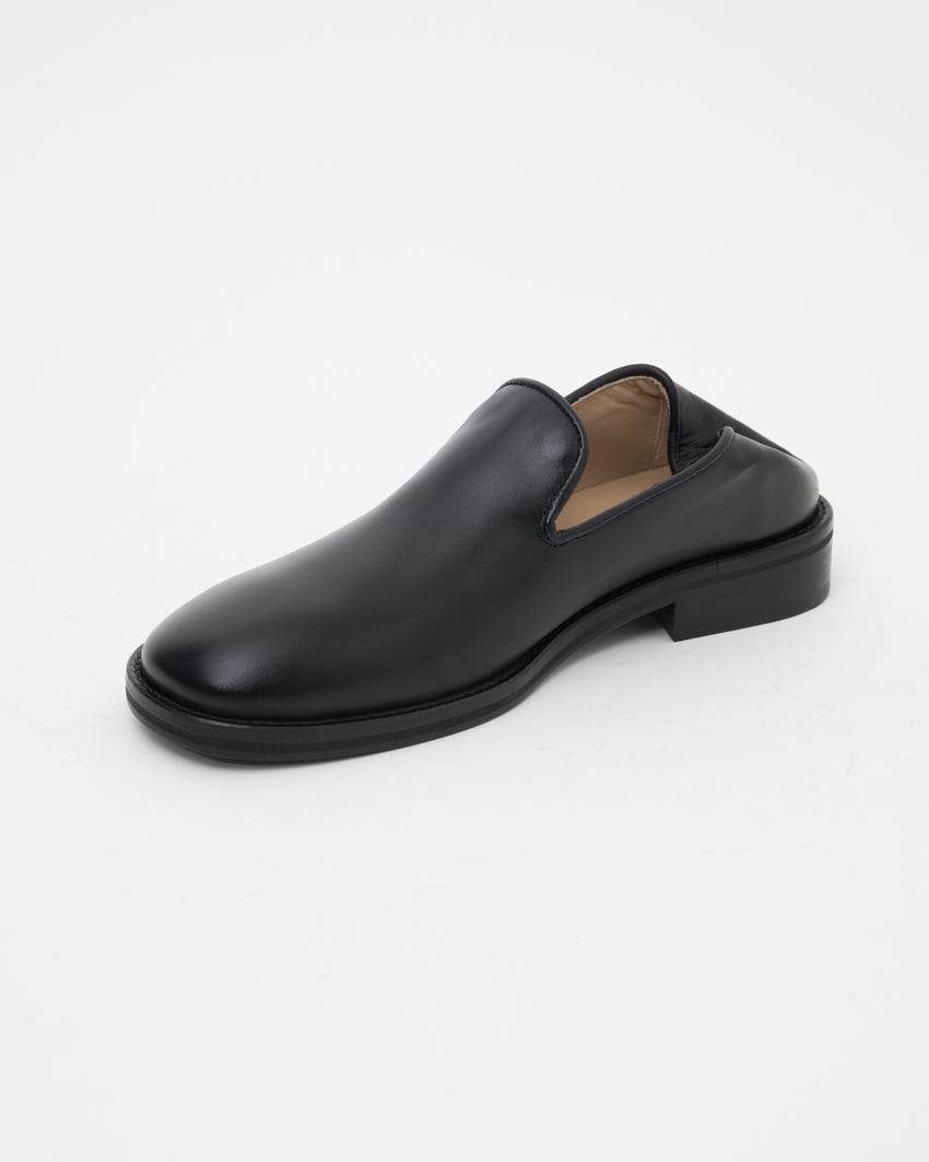 Front-angled view of single Legacy Slipper worn backless, heel folded down in slipper mode, in black calfskin leather