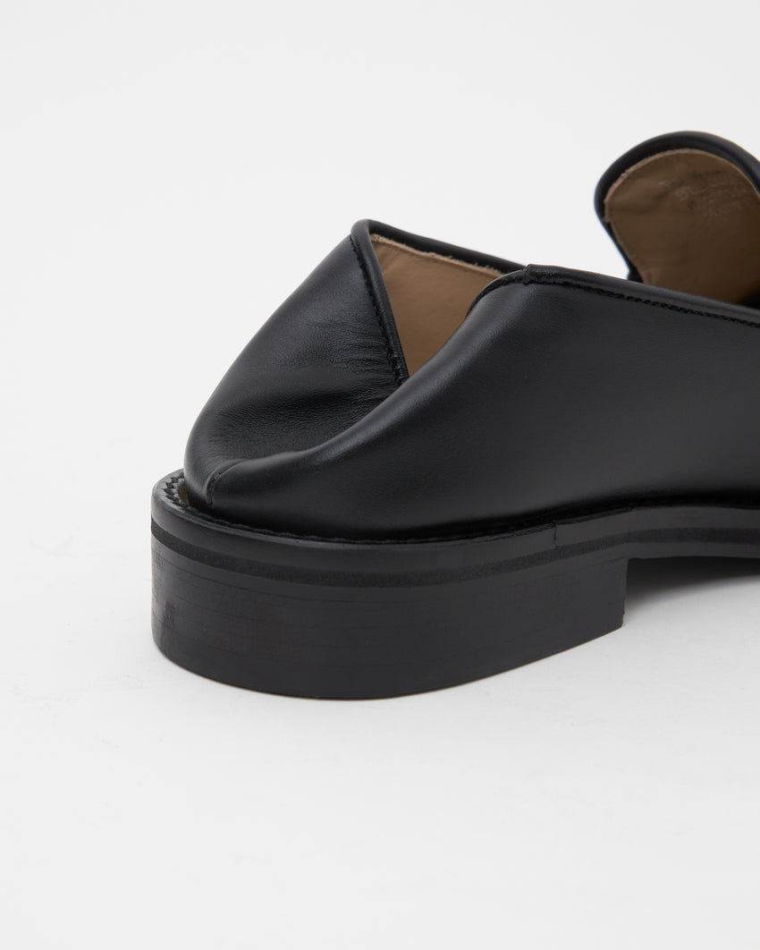 Close-up rear view of single Legacy Slipper worn backless, heel folded down in slipper mode, in black calfskin leather.
