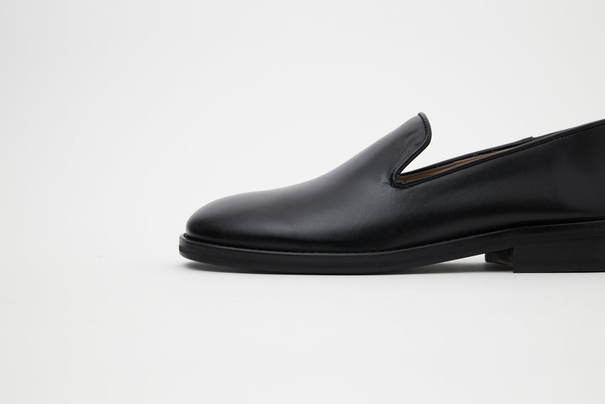 Side profile view of a single Legacy Slipper Calfskin Black loafer against a plain background