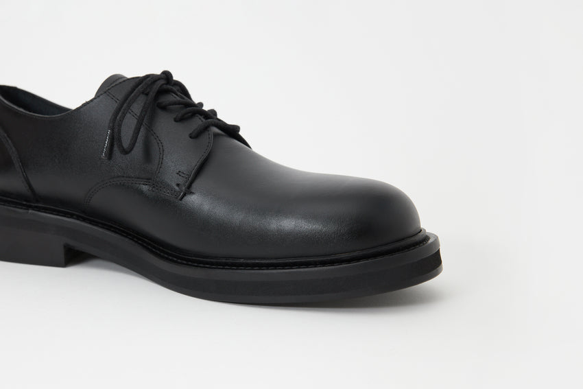 Close-up side view of the Mid-Heel Derby shoe's lace-up vamp in calfskin black