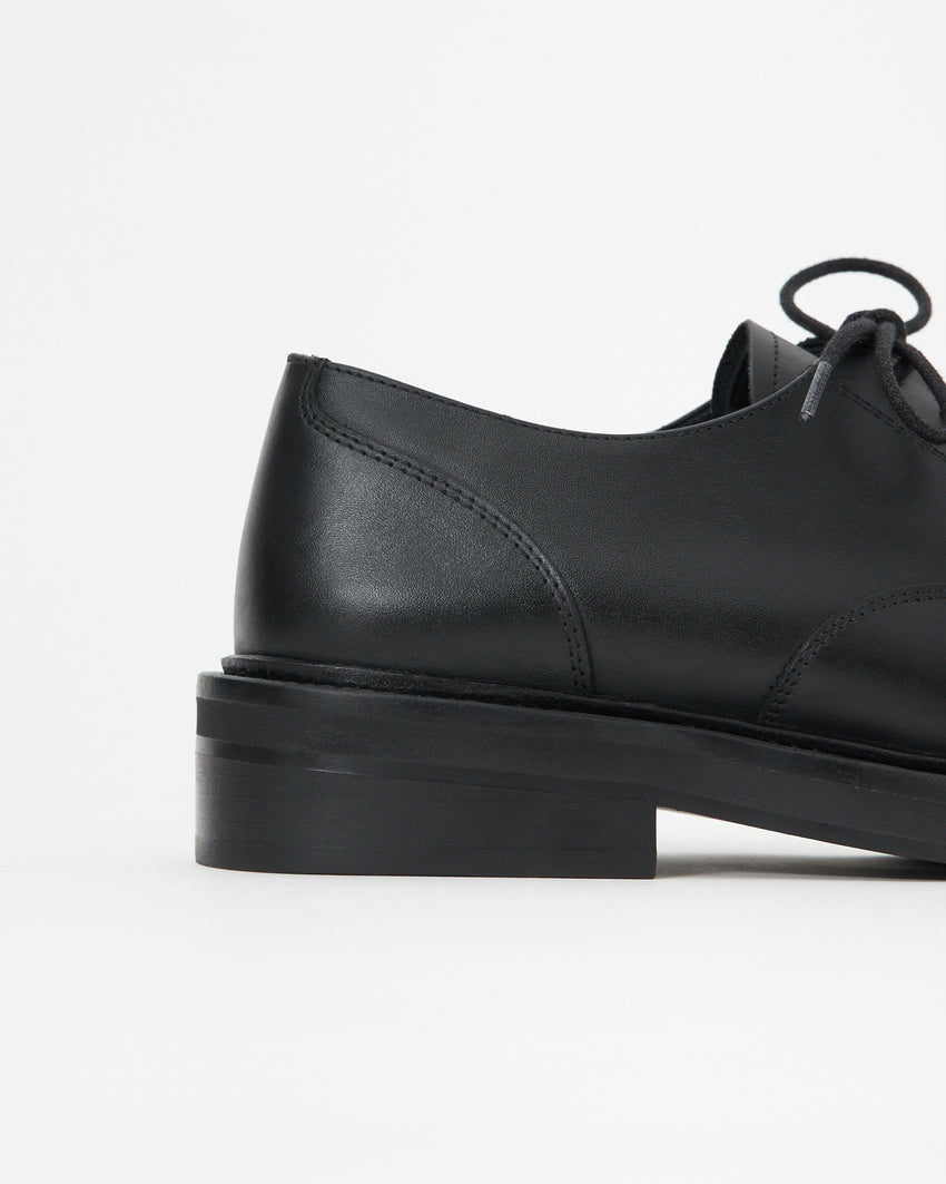 Side view of the Mid-Heel Derby shoe in calfskin black, showing the stacked block heel