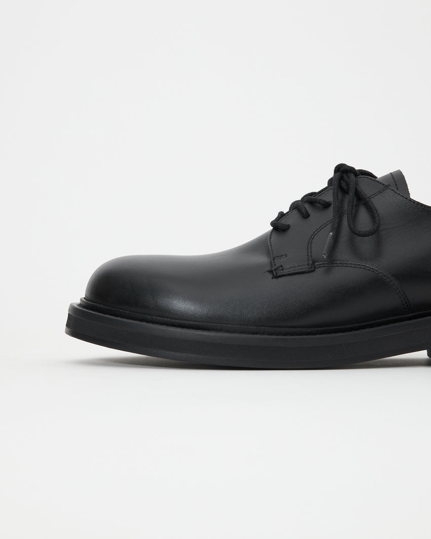 Side view of the Mid-Heel Derby shoe in calfskin black, angled to show the lace-up vamp