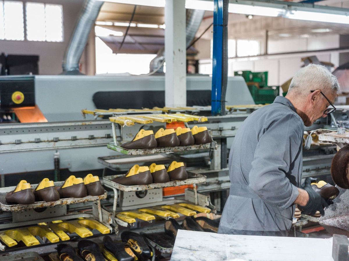 A shoemaker at work beside racks of slippers on lasts